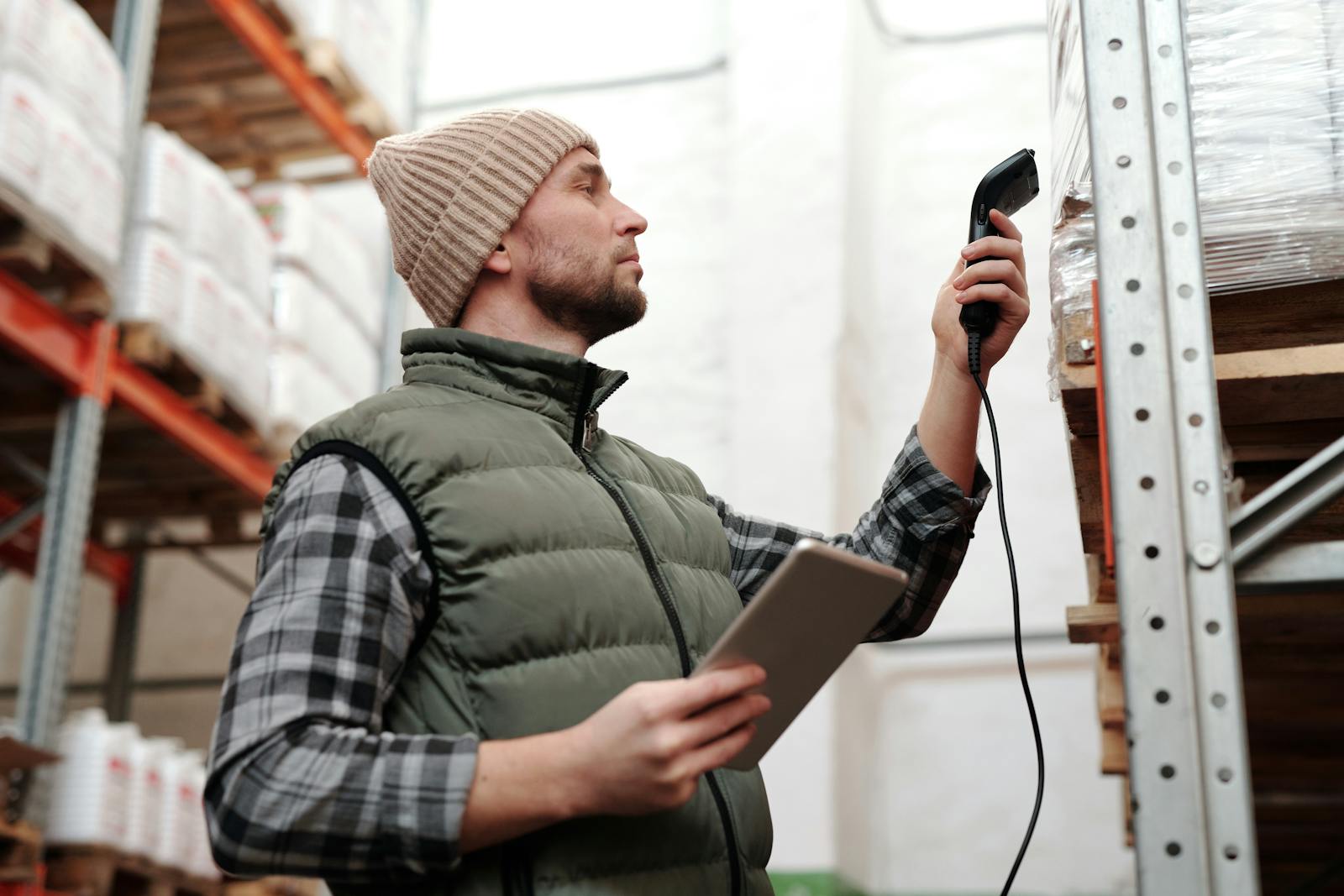 Male warehouse staff scanning inventory with handheld scanner and tablet indoors.